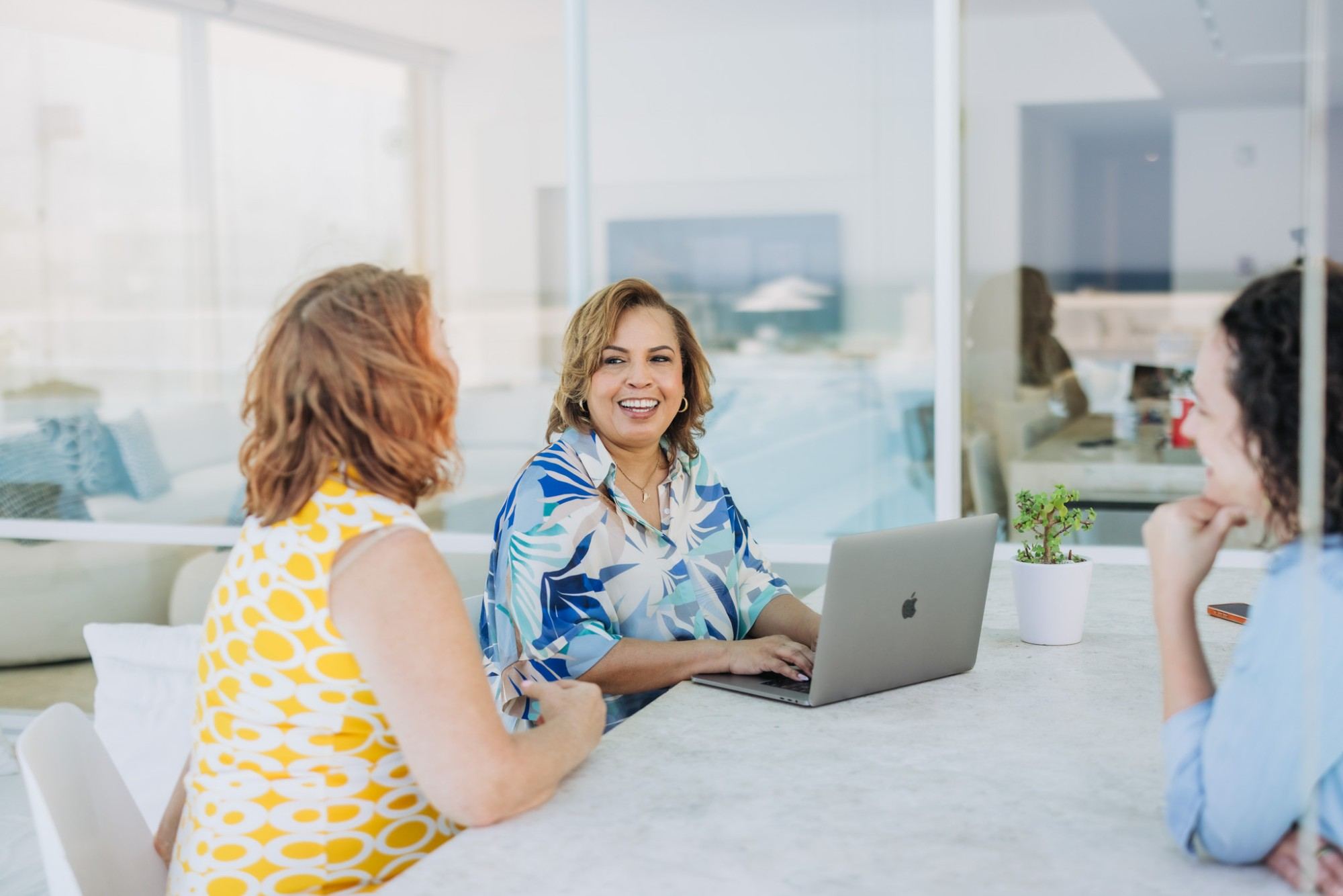 Tanya Blanchard laughing with two clients at a bright marble table, laptop open