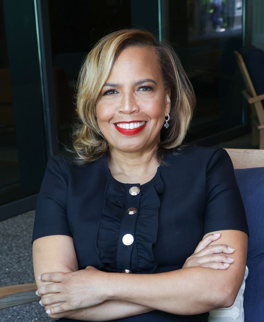 Tanya Blanchard seated in a wooden chair, arms crossed, smiling warmly